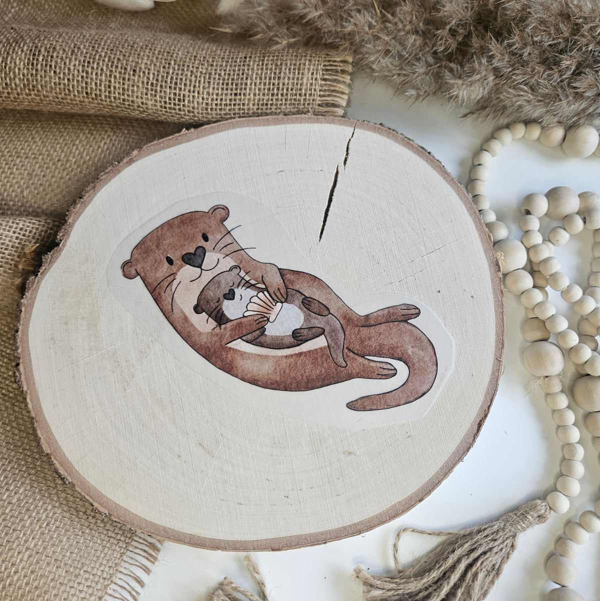 "Olli Otter" Bügelbild zum Aufbügeln – Mama-Otter hält Baby mit Muschel im Arm im Aquarellstil auf Holzscheibe, handmade | Little Falili
