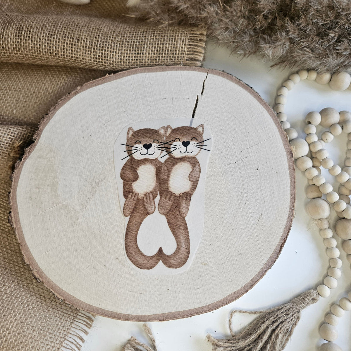 "Otterliebe" Bügelbild zum Aufbügeln – zwei verliebte Otter halten sich an den Pfoten und formen ein Herz im Aquarellstil auf Holzscheibe, handmade | Little Falili
