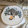 "Rentier Hütte" Bügelbild zum Aufbügeln – niedliches Rentier am Lagerfeuer vor verschneiter Holzhütte mit Tannenbäumen im Aquarellstil auf Holzscheibe, handmade | Little Falili
