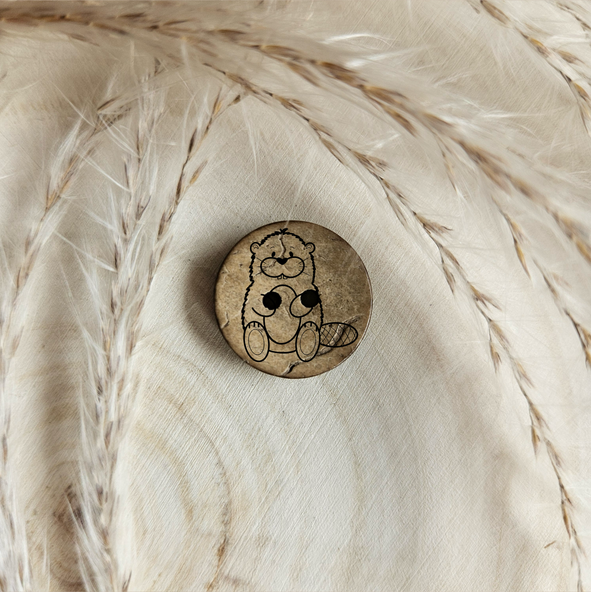 Runder Kokosknopf mit Bibermotiv auf einer hellen Holzscheibe im natürlichen Boho-Stil.