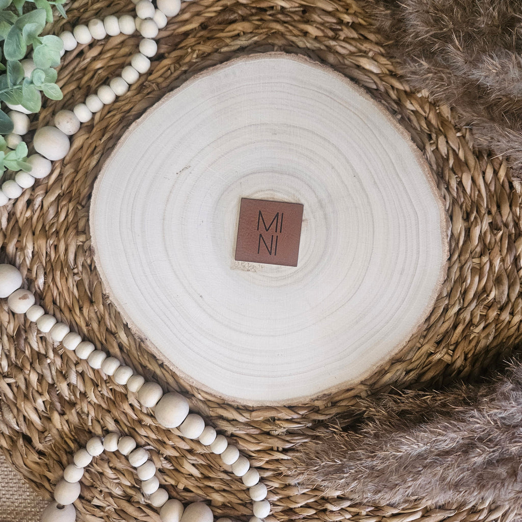 Braunes PU-Kunstlederlabel mit dem Schriftzug „MINI“  auf einer hellen Holzscheibe im natürlichen Boho-Stil.