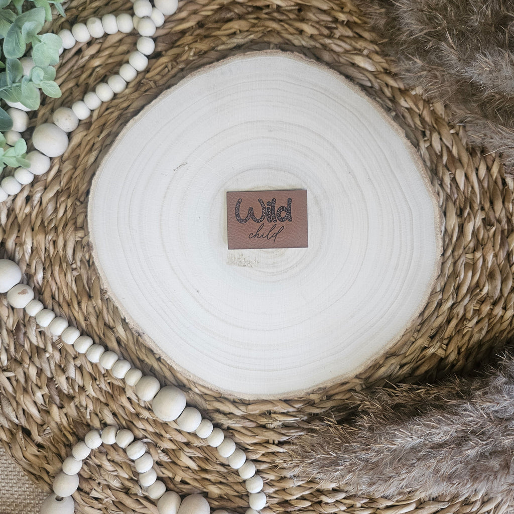 Braunes PU-Kunstlederlabel mit dem Schriftzug „Wild Chrildr“  auf einer hellen Holzscheibe im natürlichen Boho-Stil.