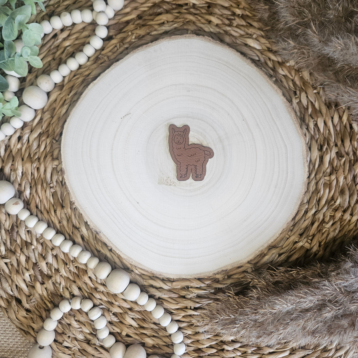 Braunes PU-Kunstlederlabel mit dem Schriftzug „Lama“ auf einer hellen Holzscheibe im natürlichen Boho-Stil.