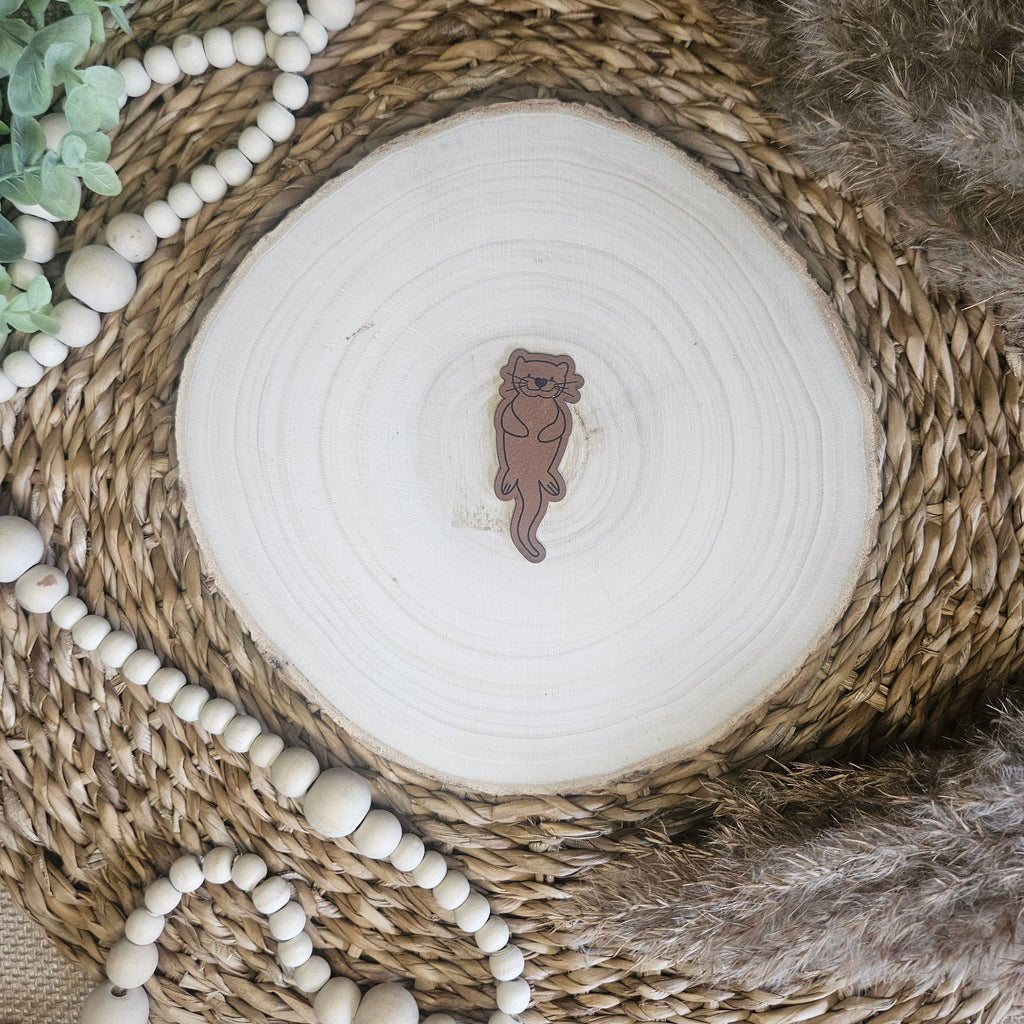 Braunes PU-Kunstlederlabel mit dem Schriftzug „Otter“ auf einer hellen Holzscheibe im natürlichen Boho-Stil.