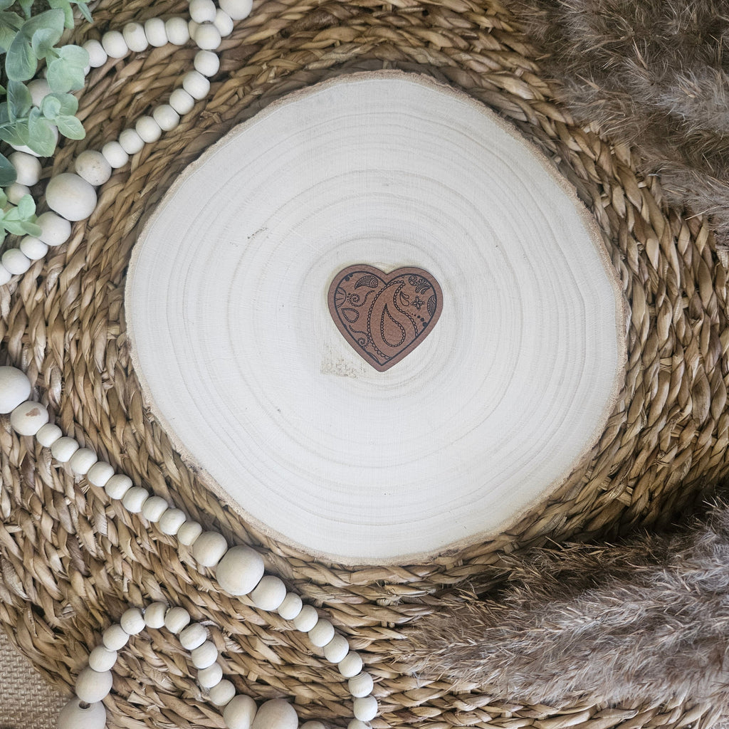 Braunes PU-Kunstlederlabel mit dem Schriftzug „Paisley Herz“ auf einer hellen Holzscheibe im natürlichen Boho-Stil.