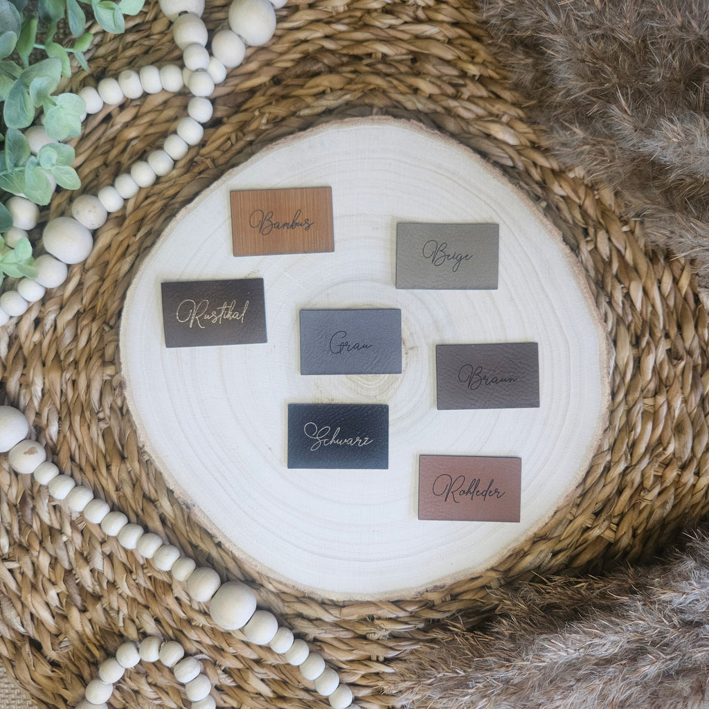 Verschiedene Farbvarianten der Kunstlederlabel auf Holzscheibe mit Boho Hintergrund