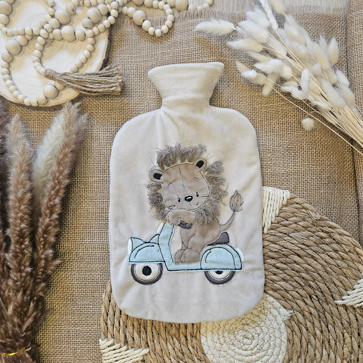 Wärmflasche mit beigem Minky-Fleece-Bezug und Löwen-Applikation auf einem Roller